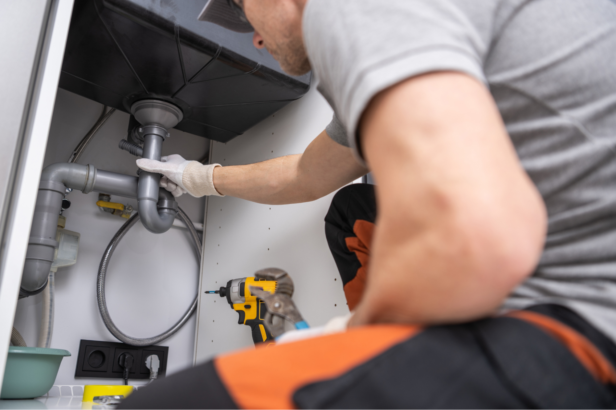 Plumber inspecting drain pipes under a kitchen sink.