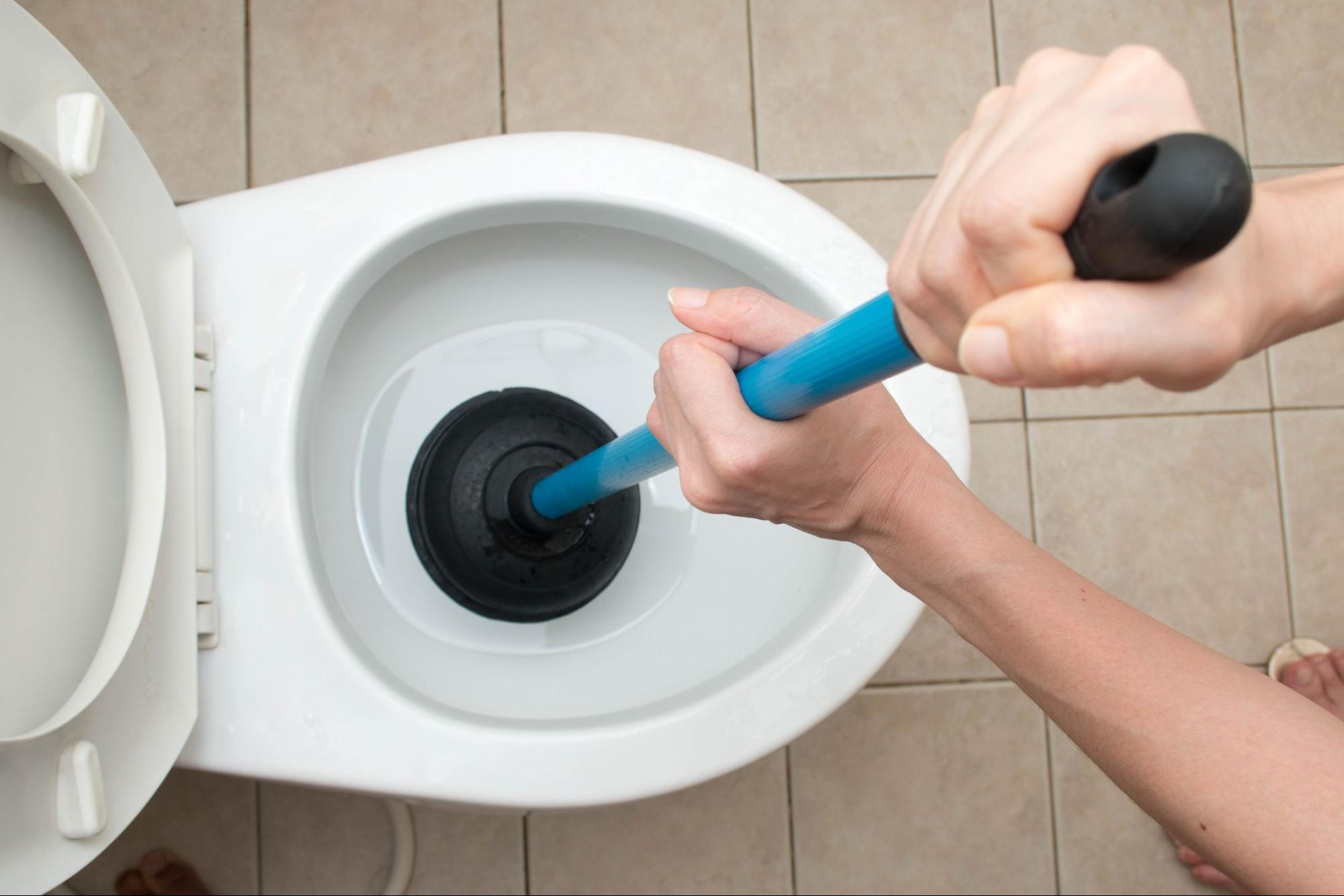 Person using a plunger inside a toilet bowl.