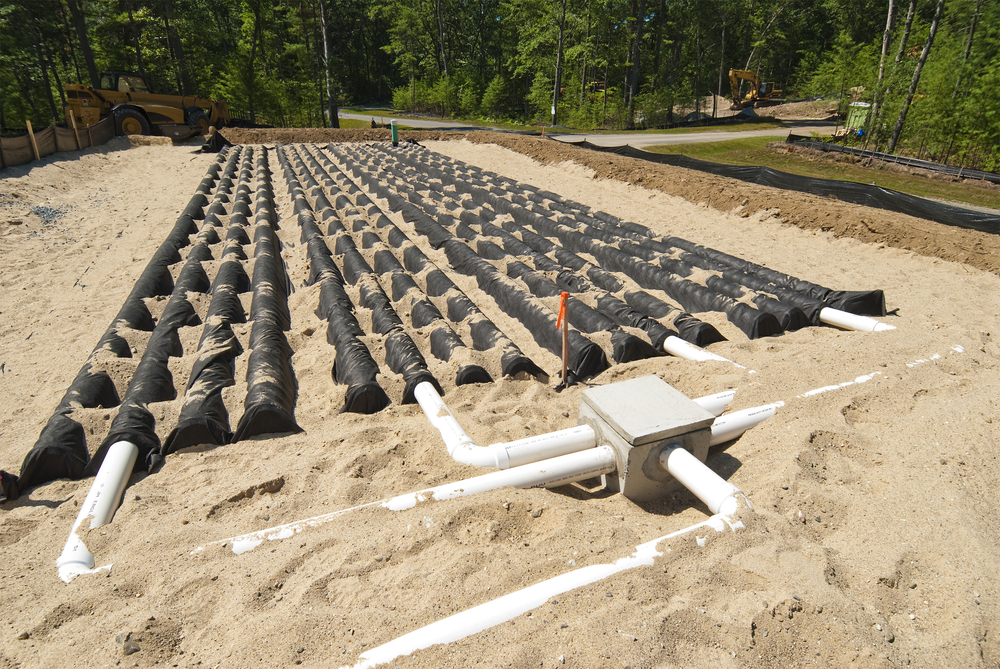 Wide view of a septic drain field with pipes and chambers on sandy soil.