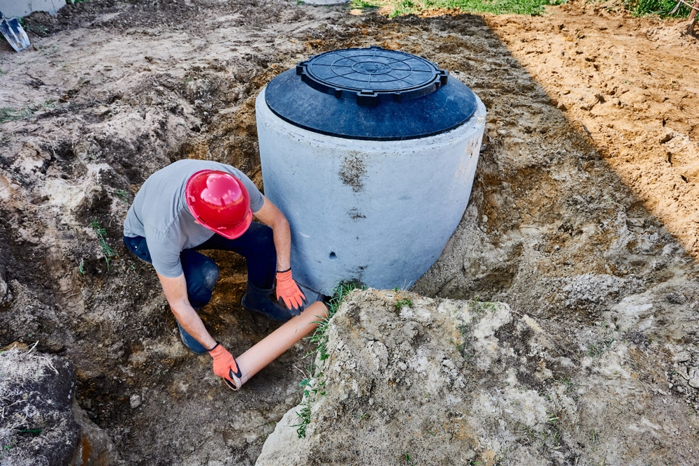 Worker connecting a pipe to a concrete septic tank.